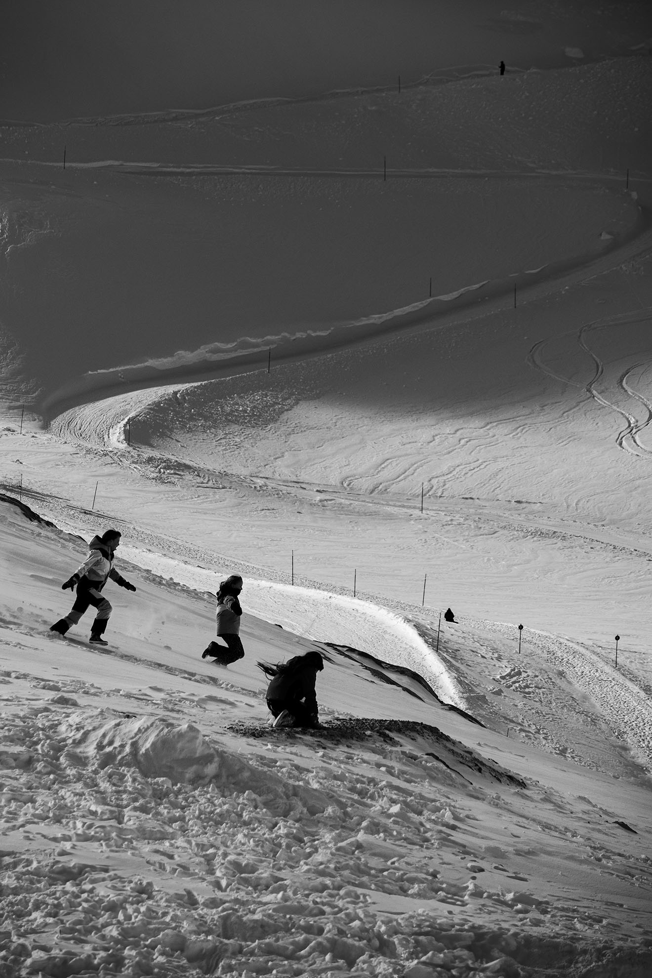 schneelandschaft mit 3 Kindern im Sprung, im Hintergrund eine Skipiste